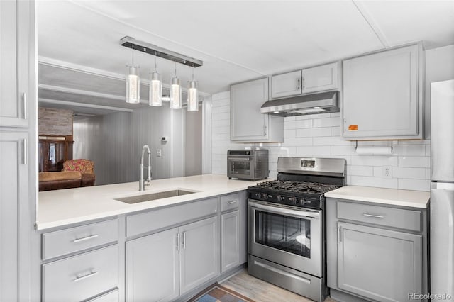 kitchen with stainless steel appliances, tasteful backsplash, gray cabinets, a sink, and under cabinet range hood