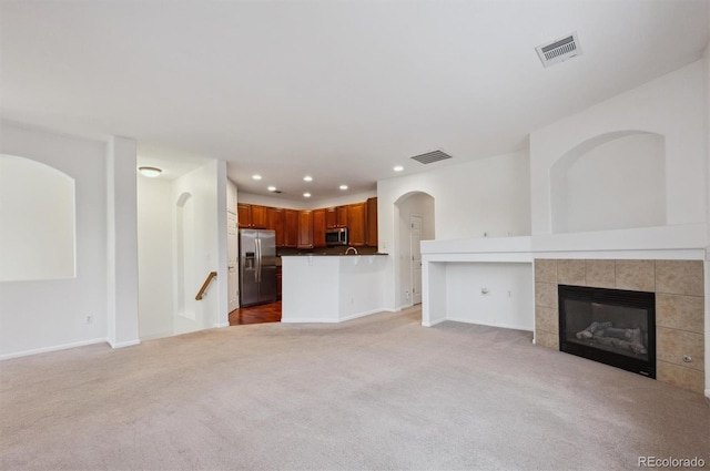 unfurnished living room with a tiled fireplace and light colored carpet