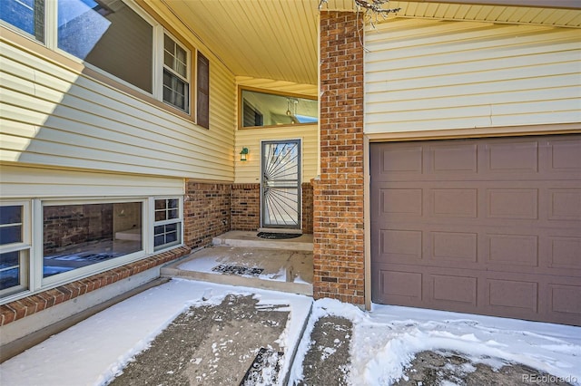 snow covered property entrance with a garage and brick siding