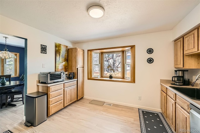 kitchen with light wood finished floors, visible vents, dishwasher, light countertops, and a sink