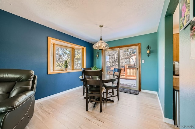 dining area featuring light wood-style floors, a textured ceiling, baseboards, and an inviting chandelier