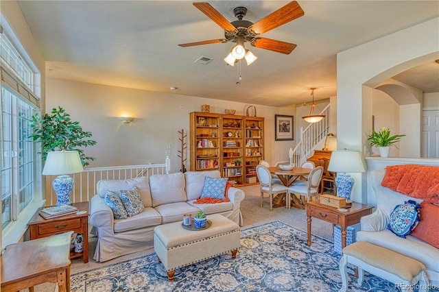 living area with arched walkways, carpet, visible vents, stairway, and ceiling fan