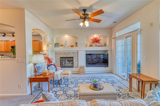 living area featuring a fireplace, light colored carpet, a ceiling fan, a textured ceiling, and baseboards