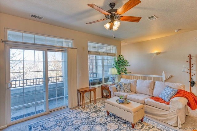 carpeted living area with a healthy amount of sunlight, visible vents, and a textured ceiling