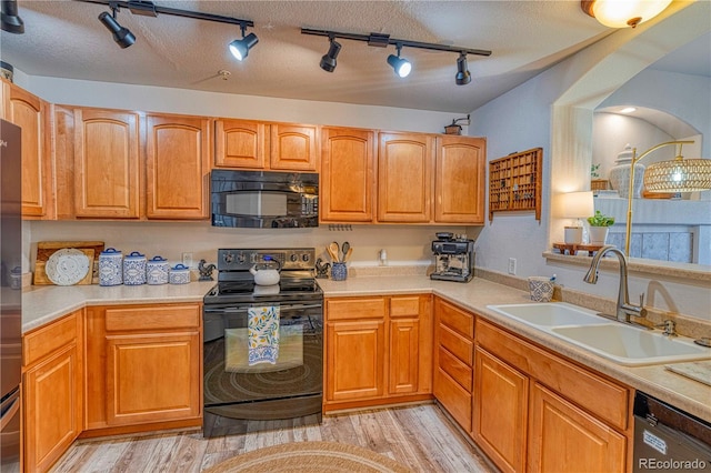 kitchen with light wood finished floors, light countertops, a sink, a textured ceiling, and black appliances