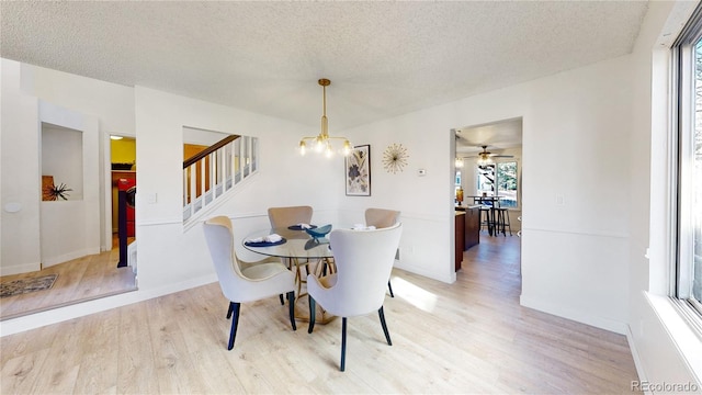 dining area with ceiling fan with notable chandelier, light wood-type flooring, and a textured ceiling