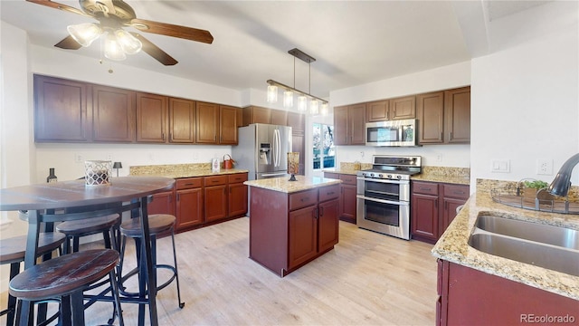 kitchen featuring sink, stainless steel appliances, pendant lighting, a kitchen island, and light wood-type flooring