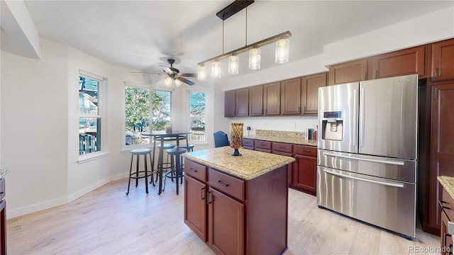 kitchen with stainless steel refrigerator with ice dispenser, light wood-type flooring, decorative light fixtures, a kitchen island, and light stone counters