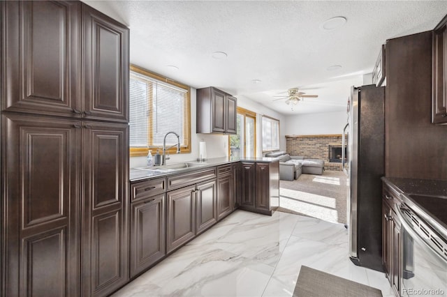 kitchen with ceiling fan, sink, a brick fireplace, a textured ceiling, and stainless steel appliances