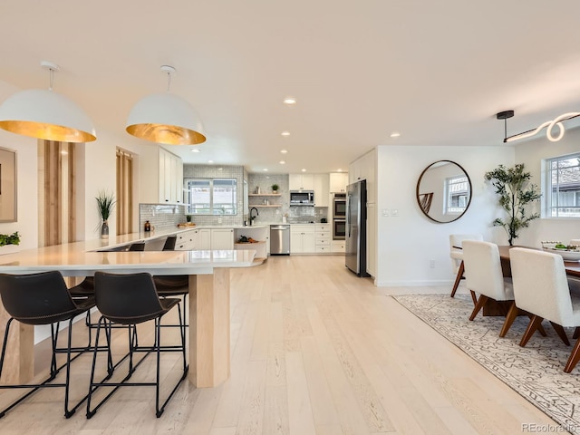 kitchen featuring stainless steel appliances, a peninsula, white cabinets, light countertops, and decorative backsplash