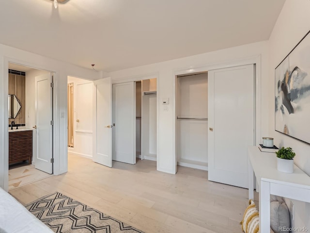 bedroom with baseboards, light wood-type flooring, connected bathroom, and multiple closets