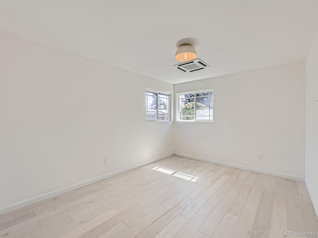 empty room with light wood-style floors, visible vents, and baseboards