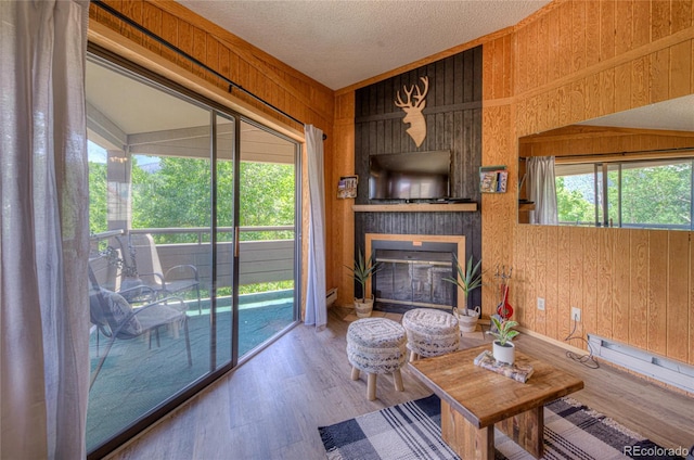 living room featuring a large fireplace, plenty of natural light, wooden walls, and wood finished floors