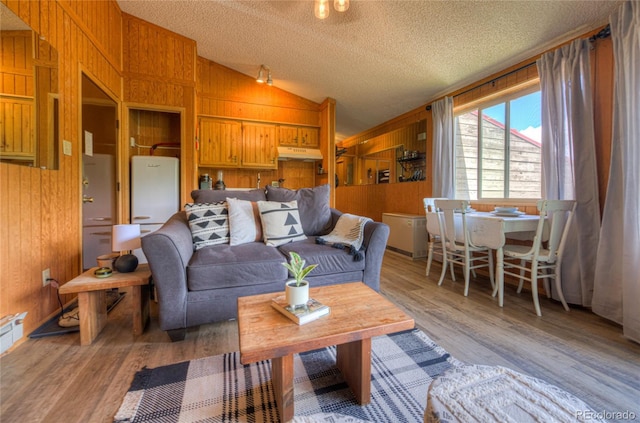 living area with lofted ceiling, wooden walls, light wood-style flooring, and a textured ceiling