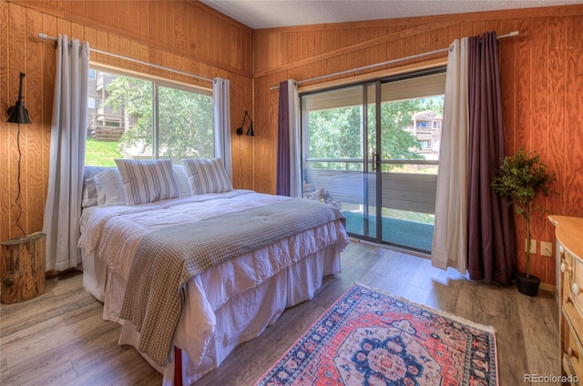 bedroom with lofted ceiling, access to exterior, wooden walls, and light wood finished floors