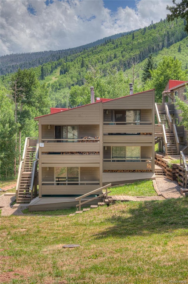 back of property with a lawn, stairway, and a forest view