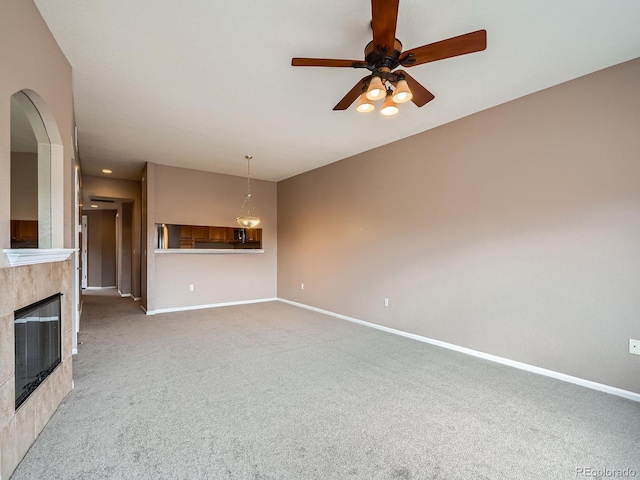 unfurnished living room featuring a tiled fireplace, carpet flooring, and ceiling fan