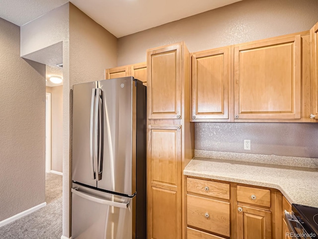 kitchen with stainless steel refrigerator, light brown cabinetry, carpet floors, and stove