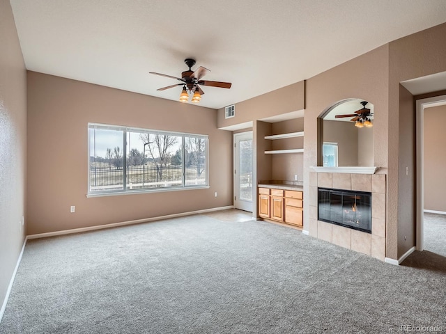 unfurnished living room featuring light carpet, a tiled fireplace, built in features, and ceiling fan