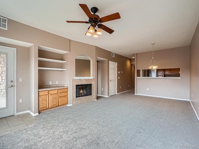 unfurnished living room featuring light carpet, built in shelves, a fireplace, and ceiling fan