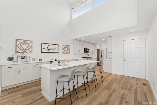 3413 W 114th Cir Unit B, Westminster, CO 80031 - kitchen with stainless steel appliances, white cabinets, light wood-style flooring, a center island, and a breakfast bar