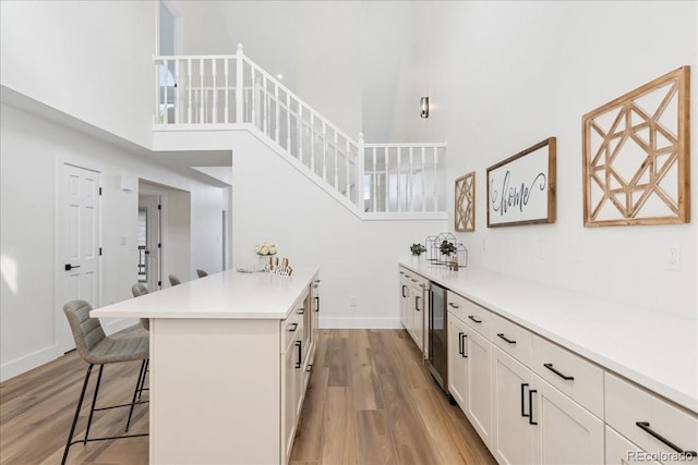 3413 W 114th Cir Unit B, Westminster, CO 80031 - kitchen featuring a towering ceiling, light wood-style floors, a breakfast bar, beverage cooler, and light countertops
