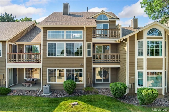 3413 W 114th Cir Unit B, Westminster, CO 80031 - back of house with a chimney, a balcony, a patio area, a lawn, and roof with shingles