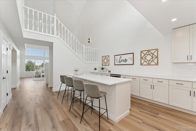 3413 W 114th Cir Unit B, Westminster, CO 80031 - kitchen with a breakfast bar area, light wood-style flooring, a towering ceiling, white cabinetry, and light countertops