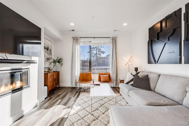 living area with recessed lighting, wood finished floors, visible vents, baseboards, and a glass covered fireplace