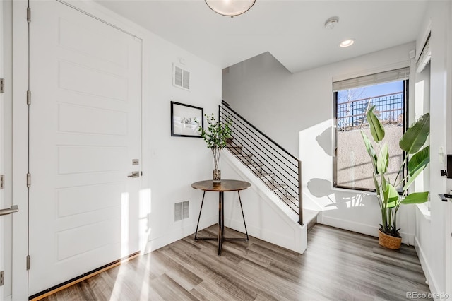 entryway with stairs, visible vents, baseboards, and wood finished floors