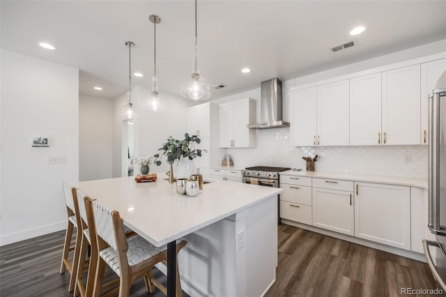 kitchen featuring visible vents, high end stainless steel range oven, decorative backsplash, white cabinets, and wall chimney exhaust hood