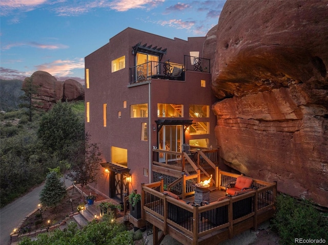 6619 Apache Pl, Larkspur, CO 80118 - back of property at dusk featuring a balcony, a wooden deck, stucco siding, an outdoor fire pit, and stairway