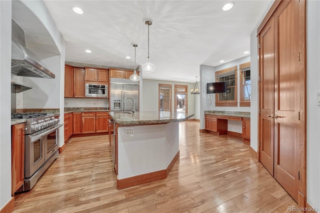 kitchen featuring a center island with sink, decorative light fixtures, high end appliances, and light stone countertops