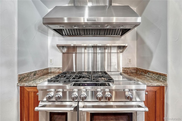 kitchen with dark stone countertops, high end range, and wall chimney range hood