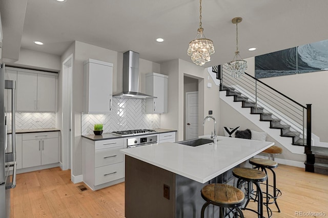 kitchen with white cabinets, light wood-type flooring, wall chimney exhaust hood, and sink