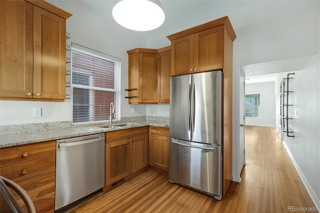 kitchen with light stone countertops, appliances with stainless steel finishes, light hardwood / wood-style flooring, and sink