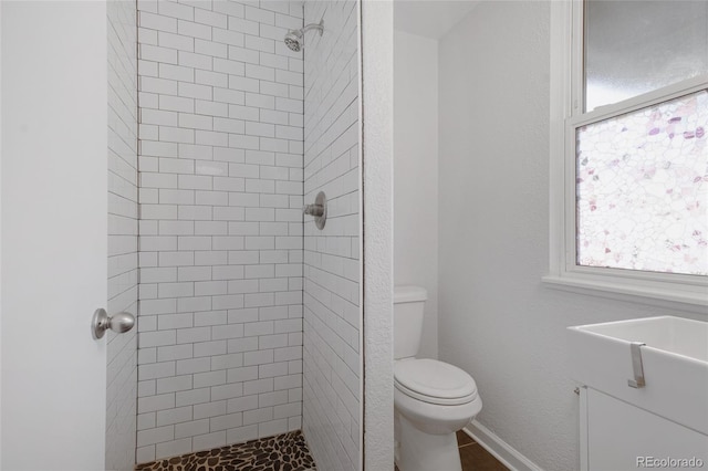 bathroom with toilet, a tile shower, and vanity