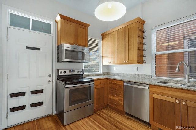 kitchen featuring stainless steel appliances, light wood-type flooring, a sink, light stone counters, and brown cabinetry