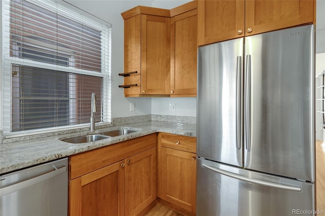 kitchen featuring stainless steel appliances, a sink, light stone counters, brown cabinetry, and light wood-style flooring
