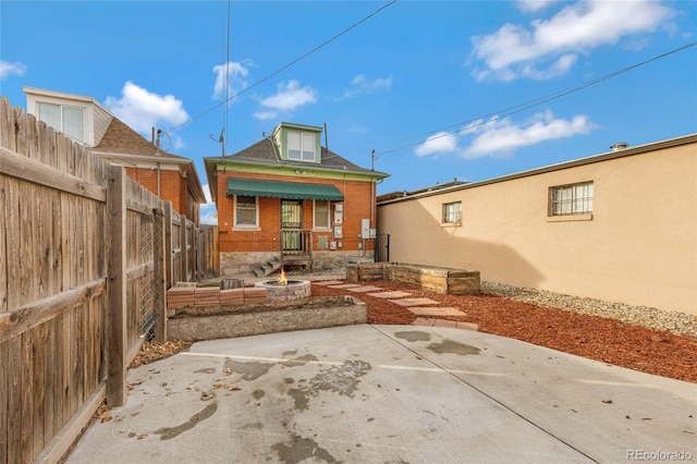 rear view of property with brick siding, a patio, and an outdoor fire pit