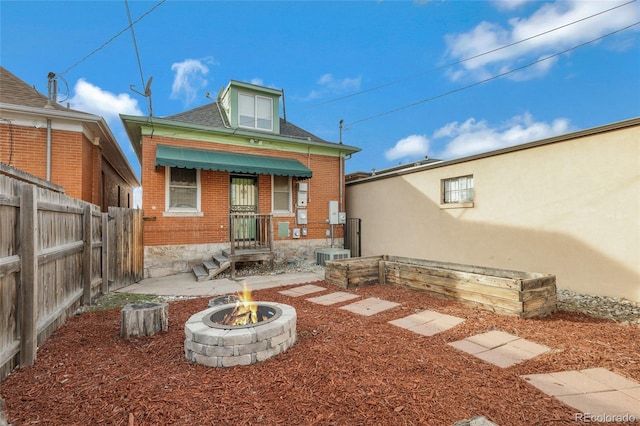 back of property with brick siding, fence, an outdoor fire pit, and cooling unit