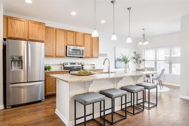 kitchen with decorative light fixtures, backsplash, stainless steel appliances, and a center island with sink