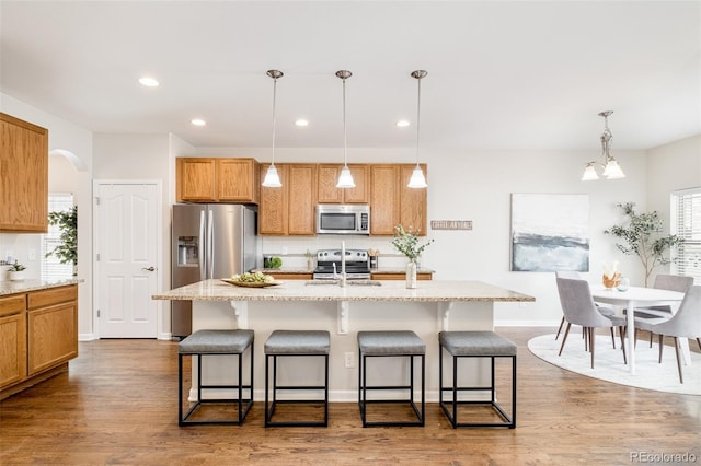 kitchen featuring appliances with stainless steel finishes, tasteful backsplash, a kitchen island with sink, dark wood-type flooring, and pendant lighting