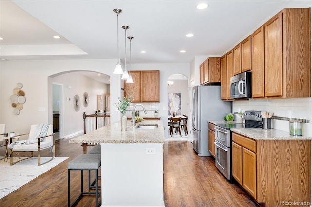 kitchen featuring appliances with stainless steel finishes, sink, decorative light fixtures, a center island with sink, and dark hardwood / wood-style floors