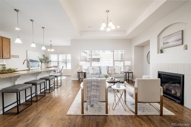 living room with a raised ceiling, sink, a notable chandelier, wood-type flooring, and a tiled fireplace