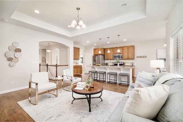 living room featuring a raised ceiling, dark hardwood / wood-style flooring, and a chandelier