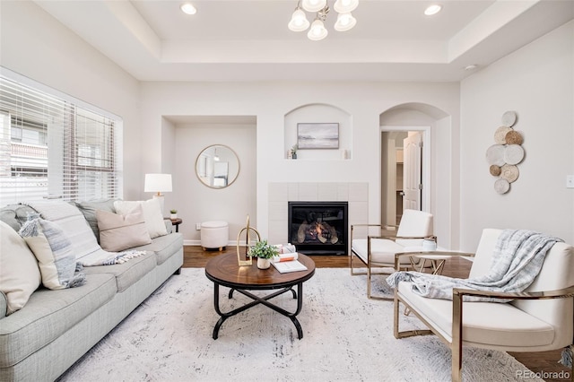 living room with a tile fireplace, hardwood / wood-style floors, a tray ceiling, and a chandelier