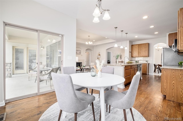 dining area featuring dark hardwood / wood-style floors, sink, a tray ceiling, and an inviting chandelier