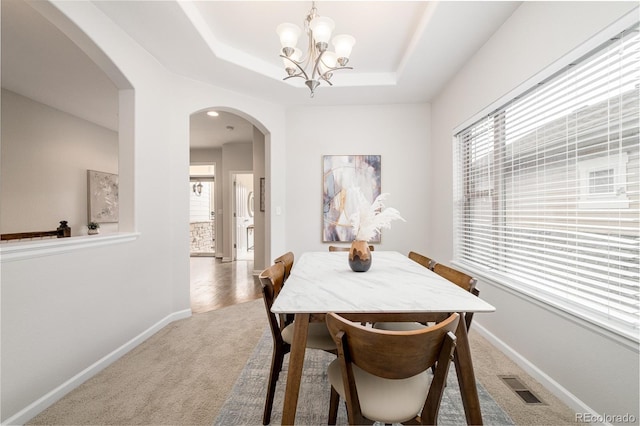 dining area with a raised ceiling, carpet floors, and a chandelier