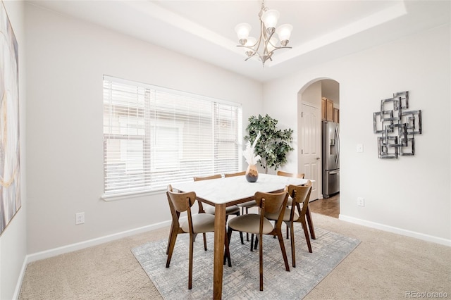 carpeted dining space featuring a raised ceiling and a notable chandelier